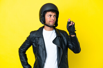 Young Brazilian man with a motorcycle helmet isolated on yellow background with fingers crossing and wishing the best