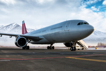 Wide body passenger jetliner and boarding stairs at the airport apron on the background of high scenic snow-capped mountains