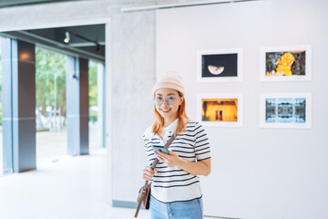 Smiling happy Woman visiting art gallery on wall watching photo frame painting at artwork museum...