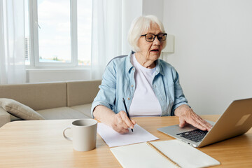 an attentive, pretty elderly woman works from home and, while studying online, makes important notes in her notebook for notes