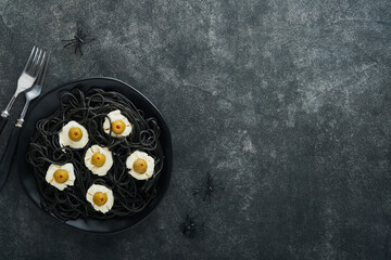 Halloween party Italian black pasta decorated horror  olives like eyes on black plate on old dark table background. Monster face from pasta. Halloween decorations and Halloween food concept. Mock up.