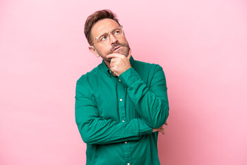 Middle age caucasian man isolated on pink background having doubts