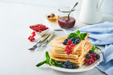 Pancakes. Stack of crepes or thin pancakes with berries, blueberries, red currants, raspberries and honey for breakfast. Homemade breakfast. Copy space. Selective focus.