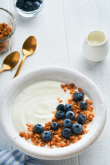 Yogurt. Greek Yogurt with granola and fresh blueberries in white bowl over old white wood background. Morning breakfast concept. Healthy food for breakfast, top view