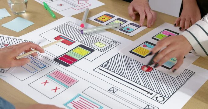 Hands of web designers creating sketches of applications for smartphones. Mobile phone interface design by design engineering team.