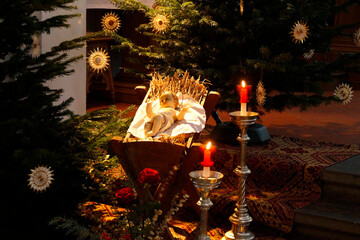 baby Jesus lying in his crib by the beautifully decorated Christmas tree surrounded by burning candles in the Catholic church in a Bavarian town (Germany)
