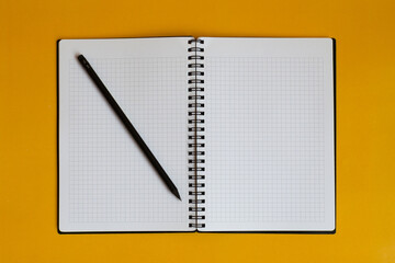 Open notebook with blank checkered pages with black pencil. Yellow background.