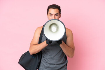 Young sport caucasian man with sport bag isolated on pink background shouting through a megaphone
