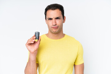 Young caucasian man holding car keys isolated on white background with sad expression