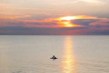 Obraz premium Silhouette of a man with two kids floating on a paddle boars in sunset hour. Pinery Provincial Park, Lake Huron, Ontario, Canada.
