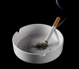 Lit cigarette in white ashtray isolated on black