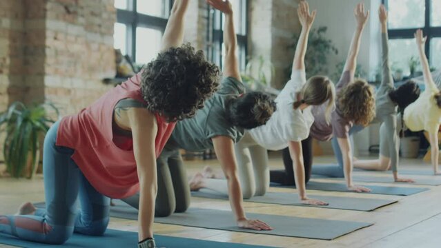 Group of women doing thread the needle stretch during yoga class with female teacher in studio