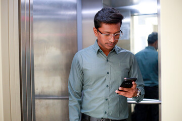 businessman using smart phone while pushing elevator button