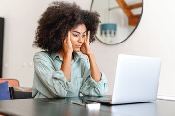 Confused black woman looking at laptop screen in despair, unemployed female looking through job...