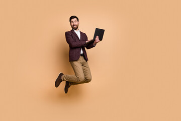 Fototapeta na wymiar Photo of active energetic jumping businessman working remotely in laptop isolated on beige color background
