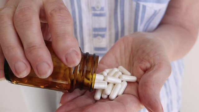 old woman pours white pills from jar into her hand, the treatment of the elderly