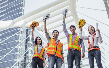 Obraz premium Group of four engineering inspectors wearing hard hat, uniform for safety, teamwork working with success, finish or complete construction, smiling with confidence, happiness, standing outdoor site.