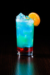 Multicolored blue-green cocktail with red jam and ice. Side view, selective focus.