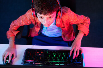 focus on kid, Top view shot of teenager kid with headphones playing video game on computer by using keyboard at home - concept of entertainment, tournament and leisure activities.