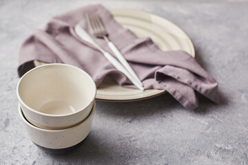 Two small empty salad bowls, plates and linen napkins on gray background