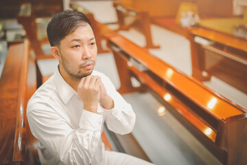 Asian man beard wearing whith shirt christian praying for blessings from god within the church...
