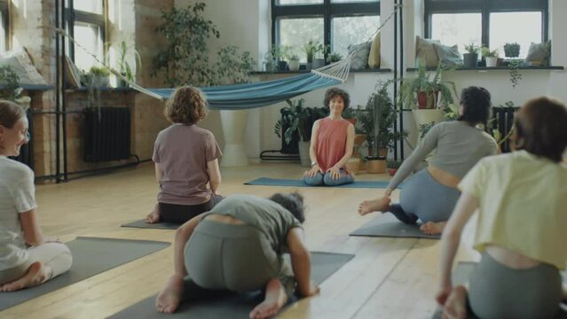 Group of women sitting in hero pose on mats during yoga practice with female teacher in studio