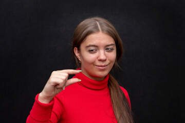 A young girl shows with her fingers the size or level of something small on a black background.