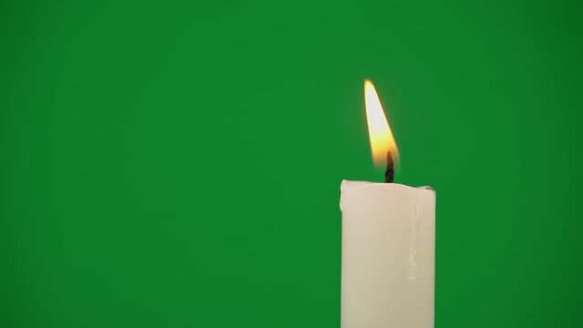 White paraffin candle with yellow tints burns on a green background. One wax candle burns motionless and emits fire.