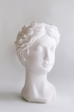 White plaster female antique statue's head on a gray background. Contemporary art. Vertical shot