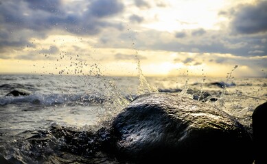 Closeup of a stone with a water pipe and windy seascape and cloudy sky in the background at sunset