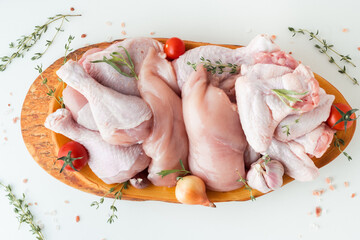 Raw uncooked chicken meat on a wooden cutting board with spices and herbs. Top view of chicken thigh, leg, fillet and wings on the white background