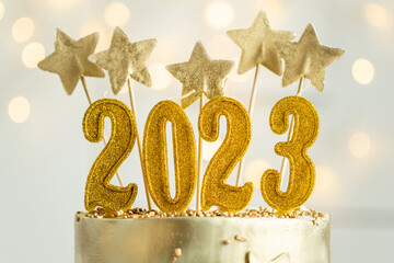 Big golden New Year cake decorated with golden stars and candles against bokeh lights background....