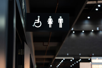 A sign of restroom lighten in white standout from a black plate. The restroom is inside a building,...