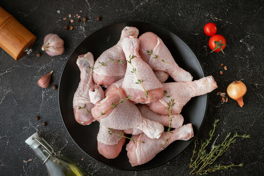 Raw uncooked chicken legs with spices and herbs in the black plate. Top view of chicken drumsticks on the black background.