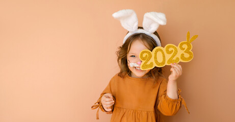 A funny laughing child in the guise of a rabbit closes his eye with the numbers 2023. The year...
