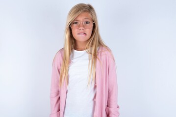caucasian blonde little girl wearing pink jacket and glasses over white background being nervous...