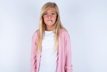 caucasian blonde little girl wearing pink jacket and glasses over white background being nervous...