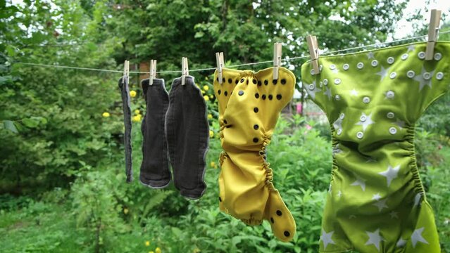Camera moves on reusable diapers are dried on clothesline outside in garden. Modern eco friendly cloth nappy for infant child hygiene. Sustainable lifestyle, zero waste concept.