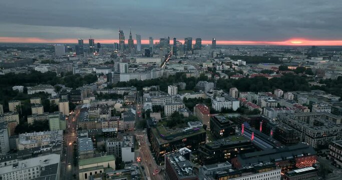 Aerial above buildings and streets in Warsaw, Polish capital at sunset. City skyline panorama with skyscrapers on the horizon. Warm orange sunlight on the horizon
