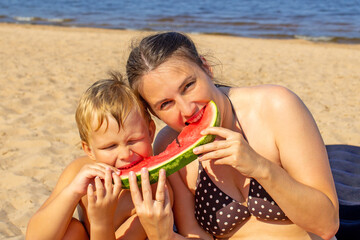 parent and child on the beach. happy mom and child bite one piece of watermelon on the background of the beach