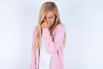 caucasian blonde little girl wearing pink jacket and glasses over white background , holding his nose because of a bad smell.