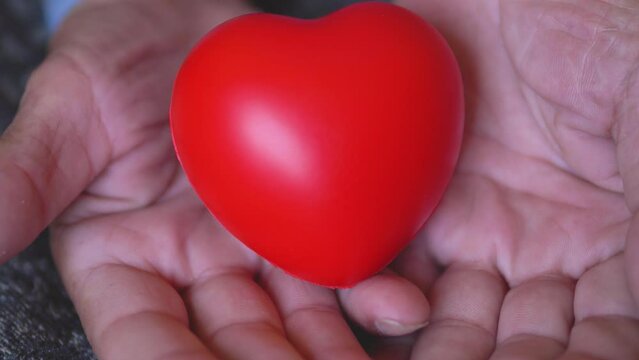 Close-up in the hands of a small red toy heart. Selective focus. Heart health of the elderly concept. Caring for the elderly. Prevention of heart attack and heart disease