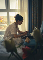 Teen girl sitting on the edge of the bed, using a laptop at home, girl chatting with friends on social networks, spending an interesting weekend, typing the text of a book, shopping online,