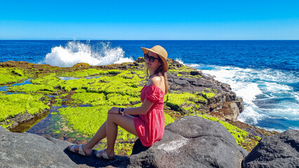 Woman with scenic view on volcanic rocks overgrown by moss, green sea plants, algae on coastline in...