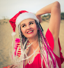 Happy middle aged attractive brunette woman in red swimsuit and Santa hat having fun on the coast. Christmas holiday vacation and travel concept.