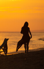 Silhouette of a sad woman walking along the beach and looking the sunset at the beach