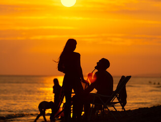 Young couple with kids smoking hookah on a beach at sunset