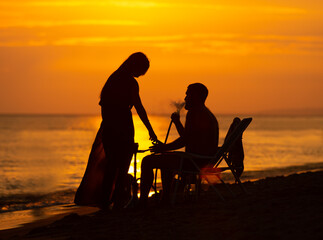 Fototapeta na wymiar Young couple with kids smoking hookah on a beach at sunset