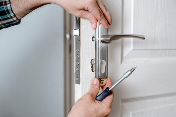 Door lock installation, repair, or replacement service. Door hardware installer locksmith working with open white door indoor - obrazy, fototapety, plakaty