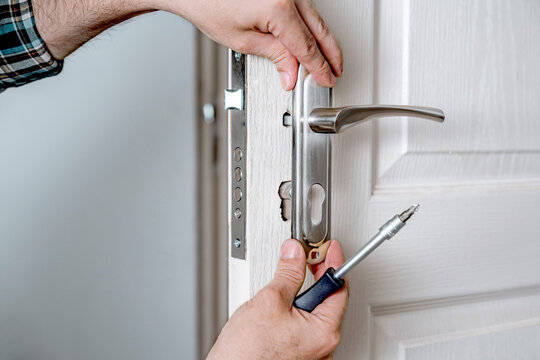 Door lock installation, repair, or replacement service. Door hardware installer locksmith working with open white door indoor